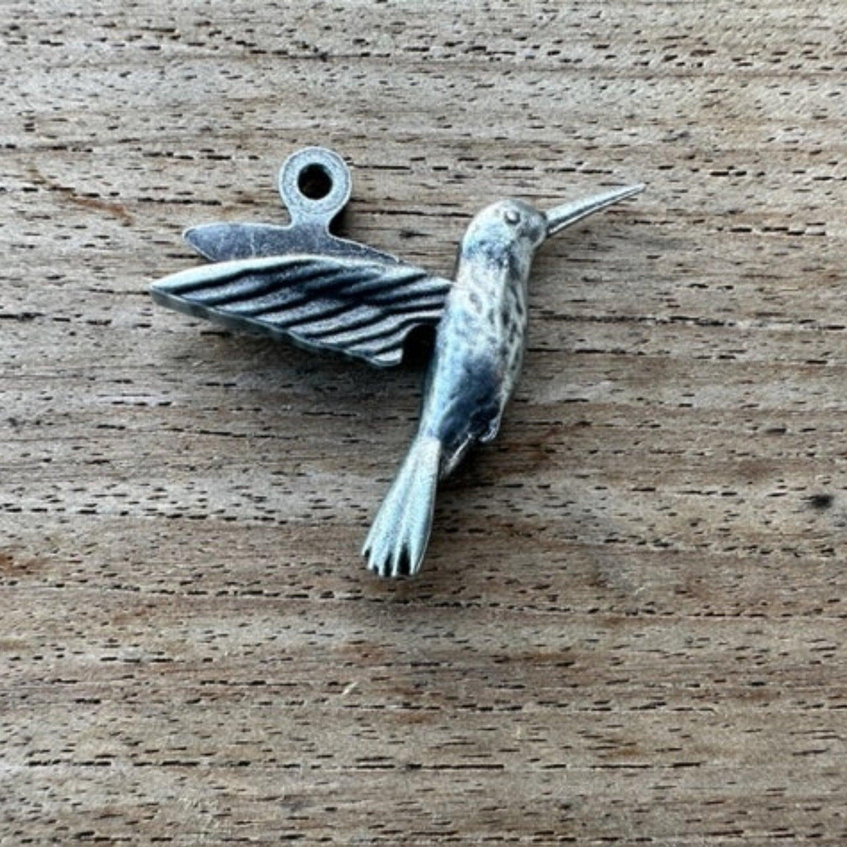 Pop's pewter hummingbird charm on a wood background
