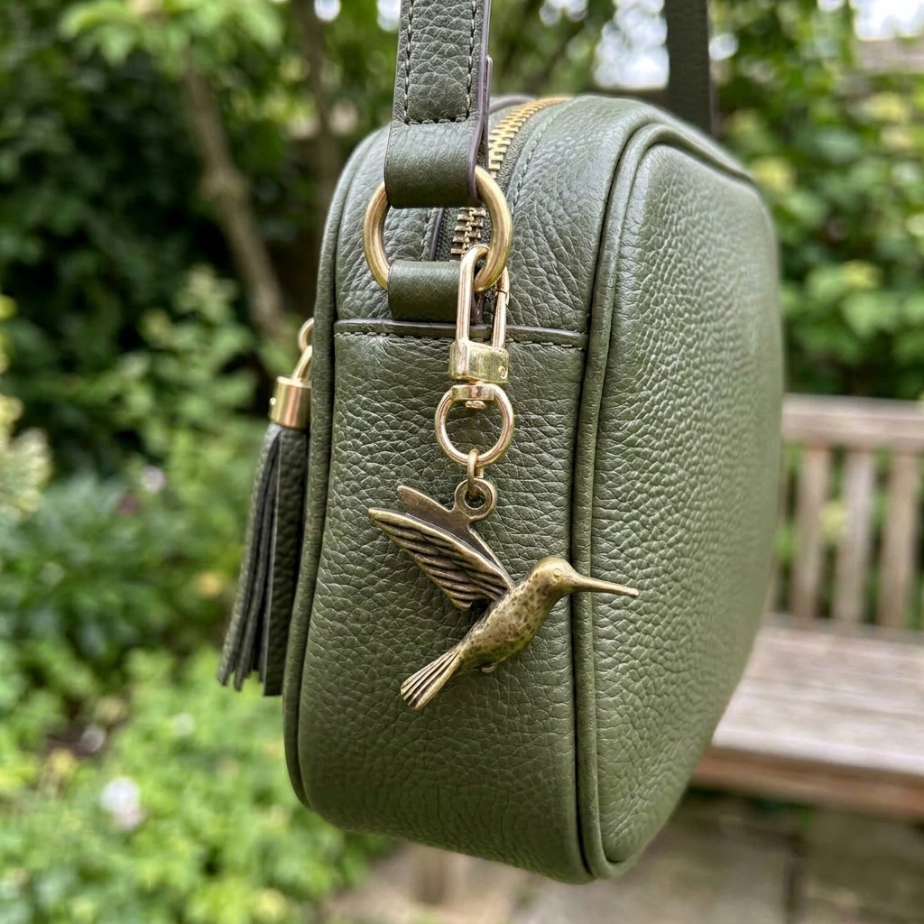 Brass hummingbird charm on a gold swivel clasp, clipped to a green leather bag