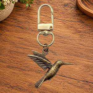 Brass hummingbird charm on a gold swivel clasp, on a wooden table