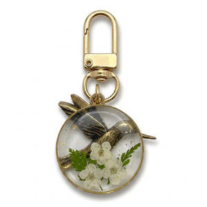 Brass hummingbird resin flower charm on a gold swivel clasp, seen at an angle