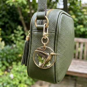 Brass hummingbird resin flower charm clipped to a green leather bag