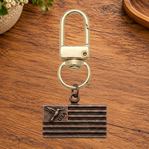 Copper USA flag charm with a hummingbird on a gold swivel clasp, on a wooden table