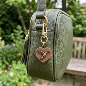 Copper heart charm with a hummingbird on a gold swivel clasp, clipped to a green leather bag