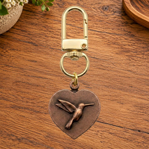 Copper heart charm with a hummingbird on a gold swivel clasp, on a wooden table