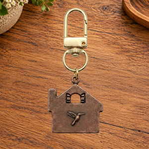 Copper home charm with a hummingbird on a gold swivel clasp, on a wooden table