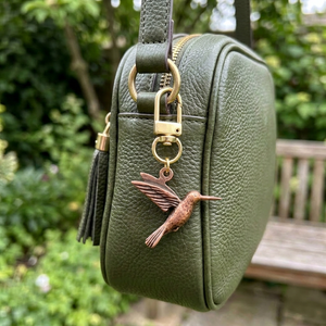 Copper hummingbird charm on a gold swivel clasp, clipped to a green leather bag