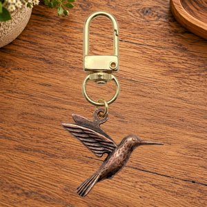 Copper hummingbird charm on a gold swivel clasp, on a wooden table