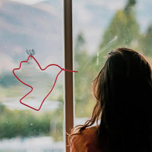 Candy Red hummingbird ornament hung on a window by a suction hook as a woman looks outside