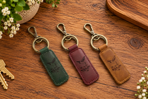 Pop's leather hummingbird keychains in forest green, burgundy and chestnut brown on a wooden table