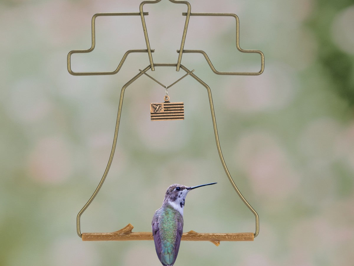 A hummingbird perched on the bronze Liberty Bell swing with its flag charm