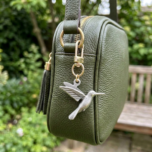 Pewter hummingbird charm on a gold swivel clasp, clipped to a green leather bag