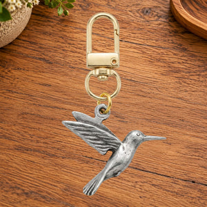Pewter hummingbird charm on a gold swivel clasp, on a wooden table