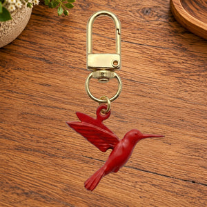 Red hummingbird charm on a gold swivel clasp, on a wooden table