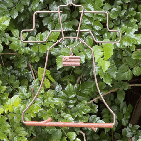 Bronze Liberty Bell hummingbird swing with flag charm hanging in front of green leaves