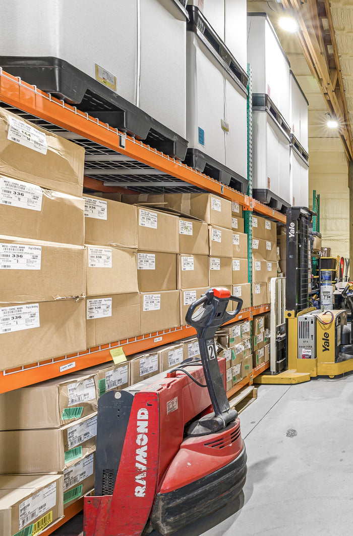Pop's warehouse aisle with cases of product on tall racks, a red pallet jack and a yellow stacker