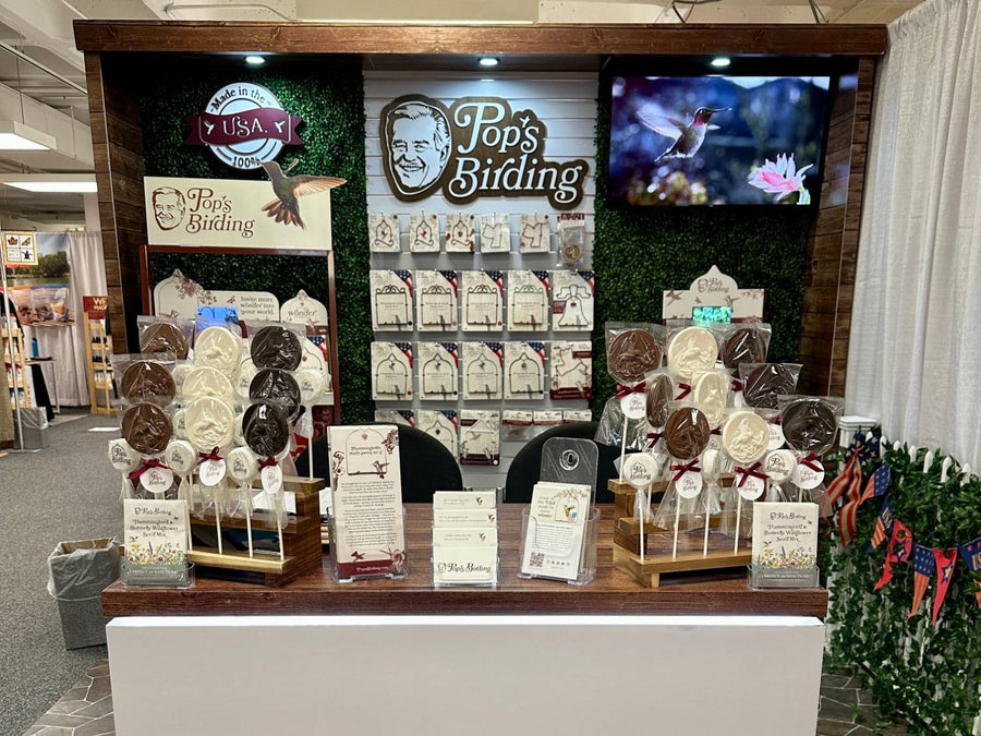 Pop's Birding portable trade show booth with the Pop's Birding logo, a hummingbird on the TV and a counter of hummingbird chocolate lollipops